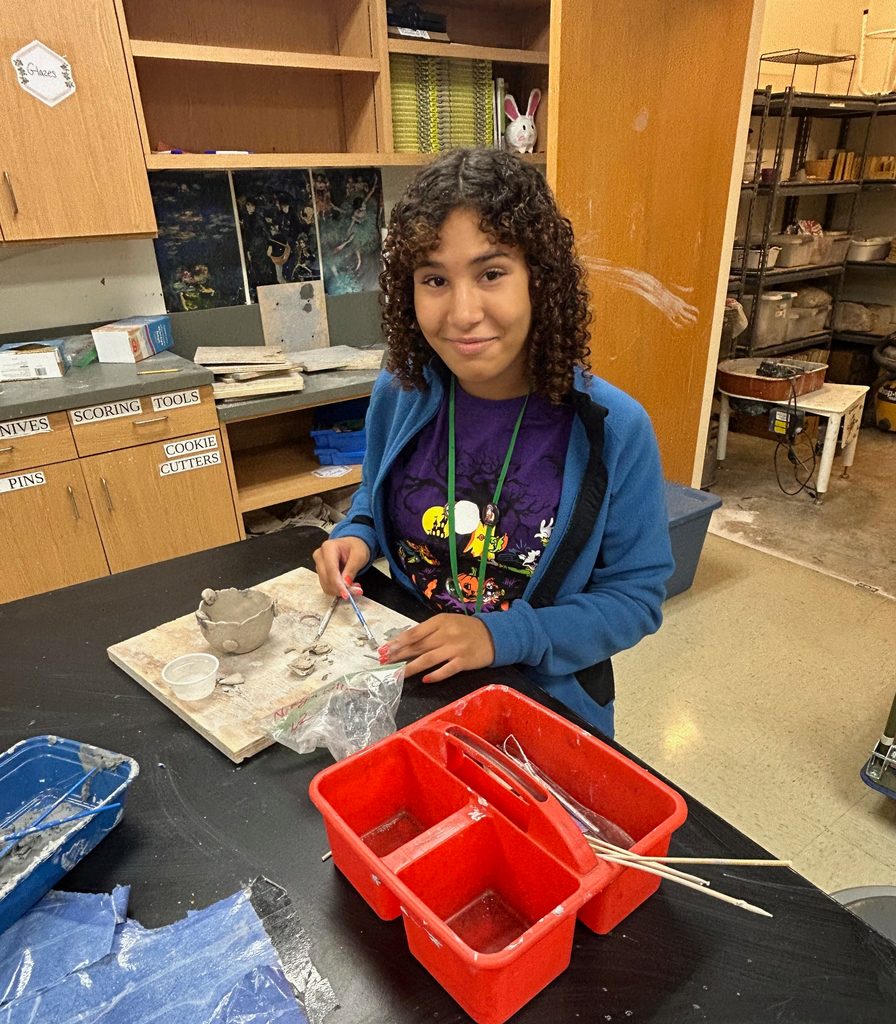 Student poses for the camera while working on their clay pinch pot project.