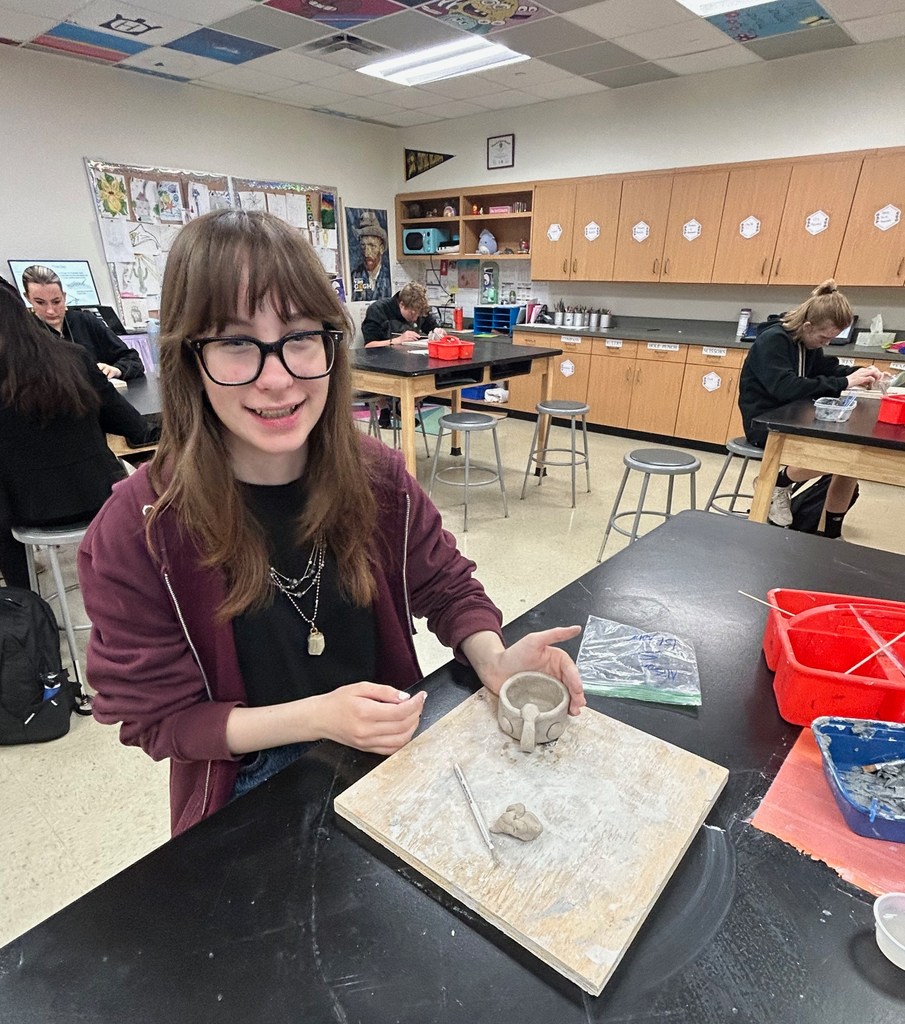 Student smiles for the camera while working on her pinch pot clay project.