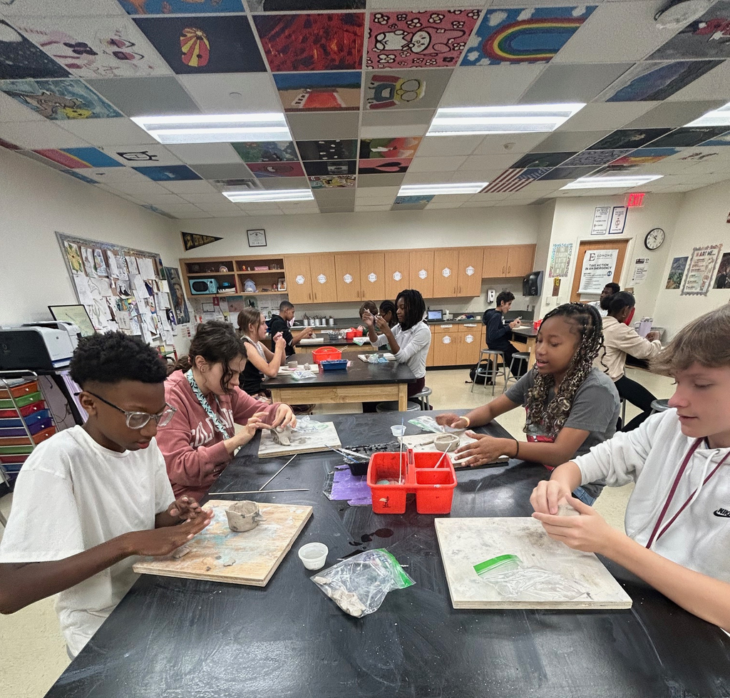 Students sit in a group at a table as they work on their clay pinch pot projects.