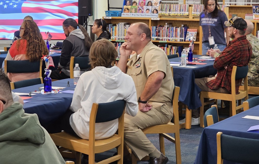 A military man dressed in uniform sitting next to a boy surrounded by tables filled with people