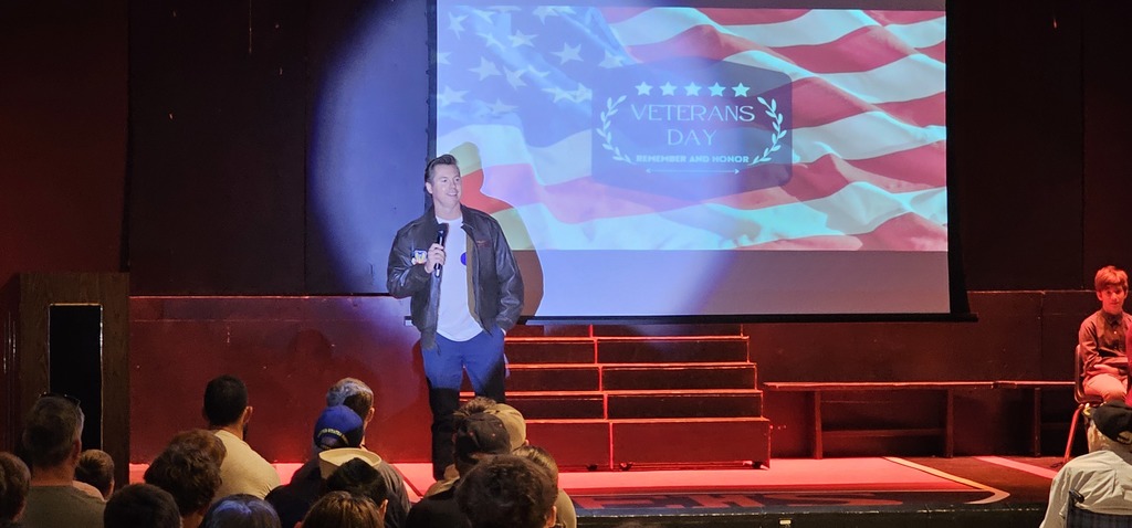Senator Pugh talking into a microphone on stage with a projector screen behind him