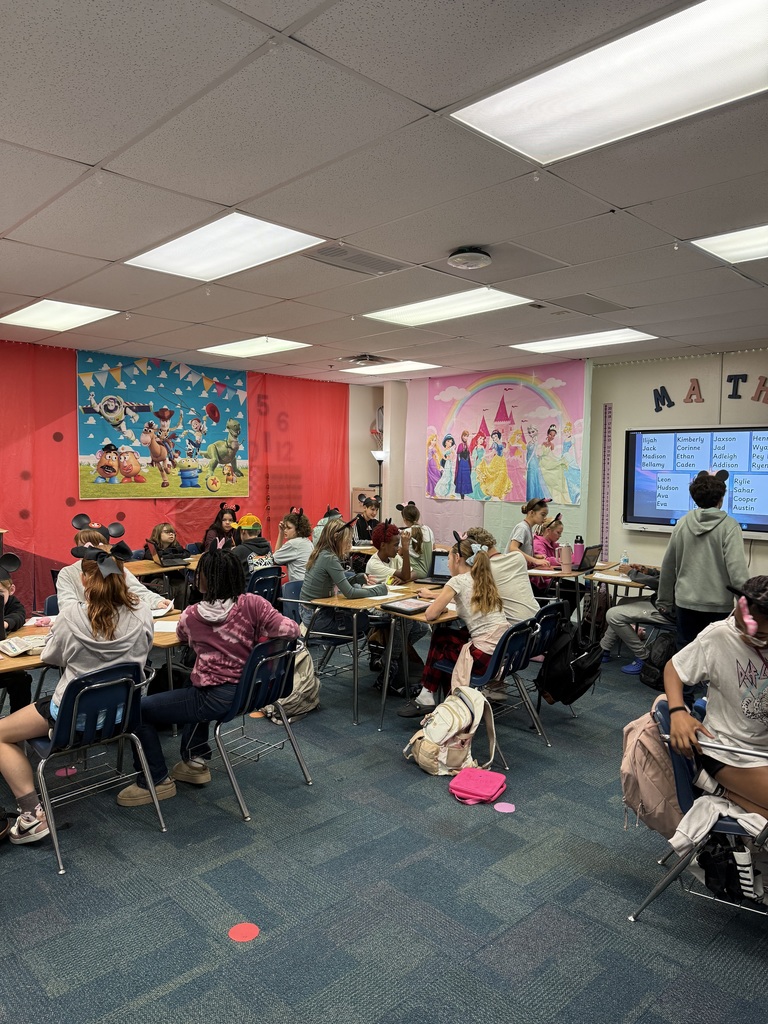 A classroom full of desks and students wearing Mickey Mouse hats with Disney themed banners in the background.