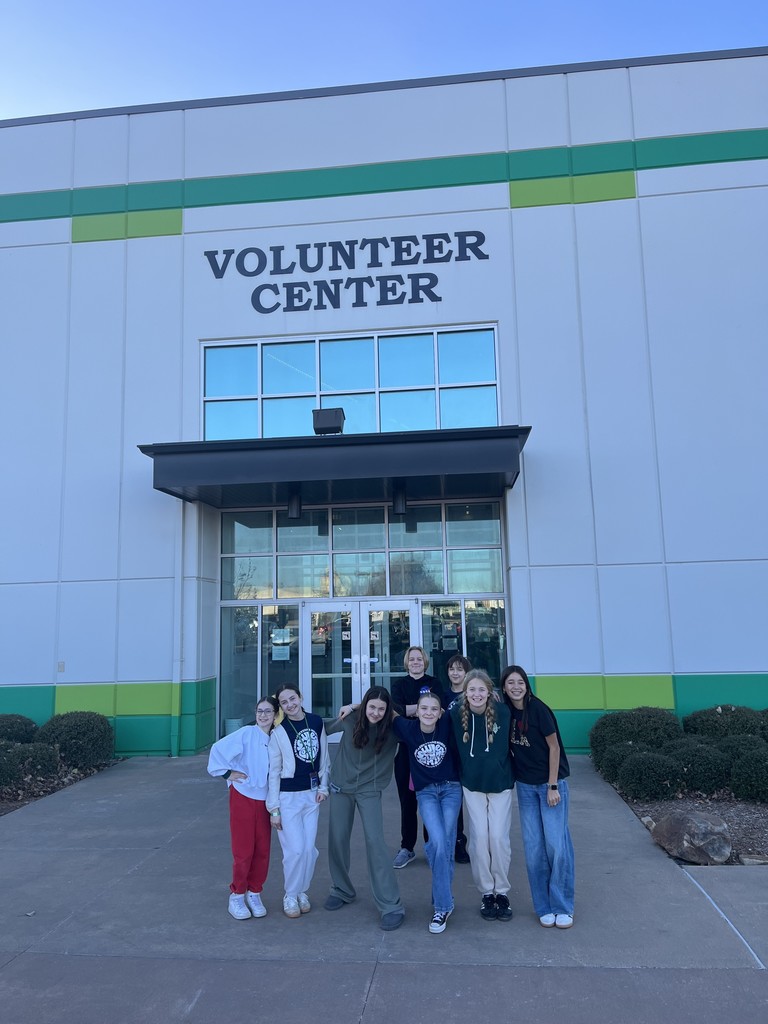 A group of students standing in front of a white and green building that says, "Volunteer Center."