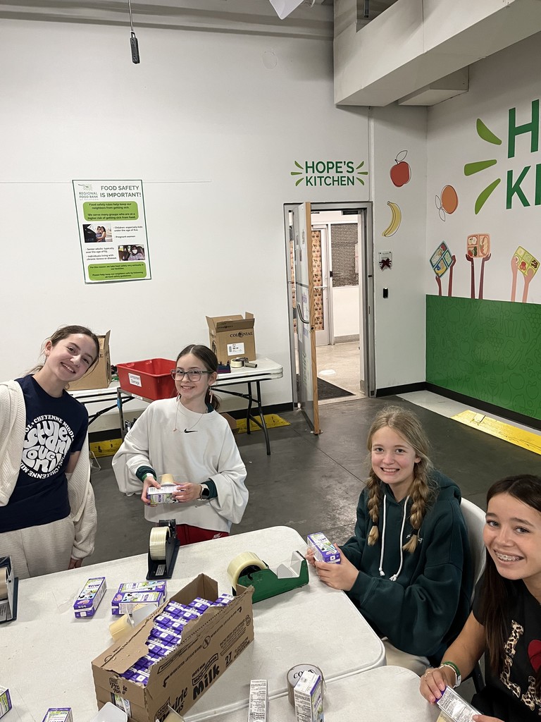 4 girls sitting at a white table wrapping milk cartons and pudding