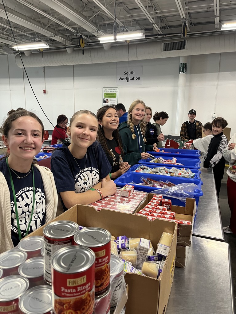 Students standing along side metal tables with various containers of non-perishable foods in front of them