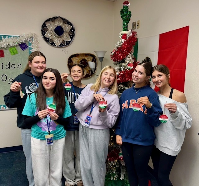 5 girls standing in a Spanish classroom holding red, white, and green colored circular ornaments