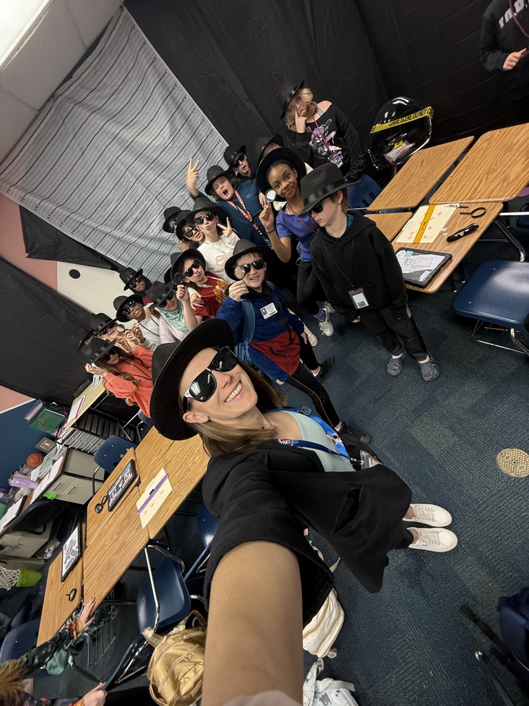 Mrs. Crutchfield taking a selfie with a group of students who are all wearing black detective hats and black sunglasses