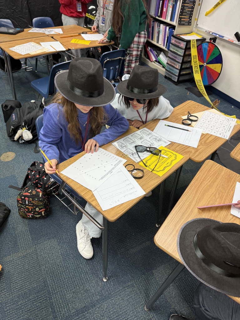 2 students looking over a paper while wearing black detective hats