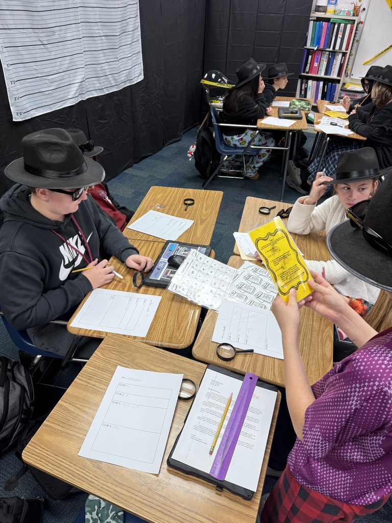 3 students sitting at desks with magnifying glasses, detective hats, and worksheets on their tables