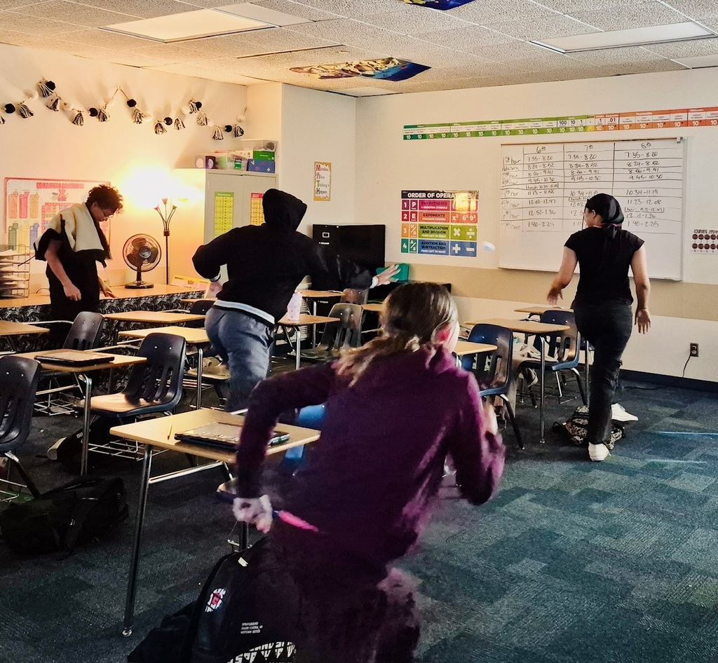 Four students are pictured in action searching for snowballs in a classroom during a Math snowball fight review game.