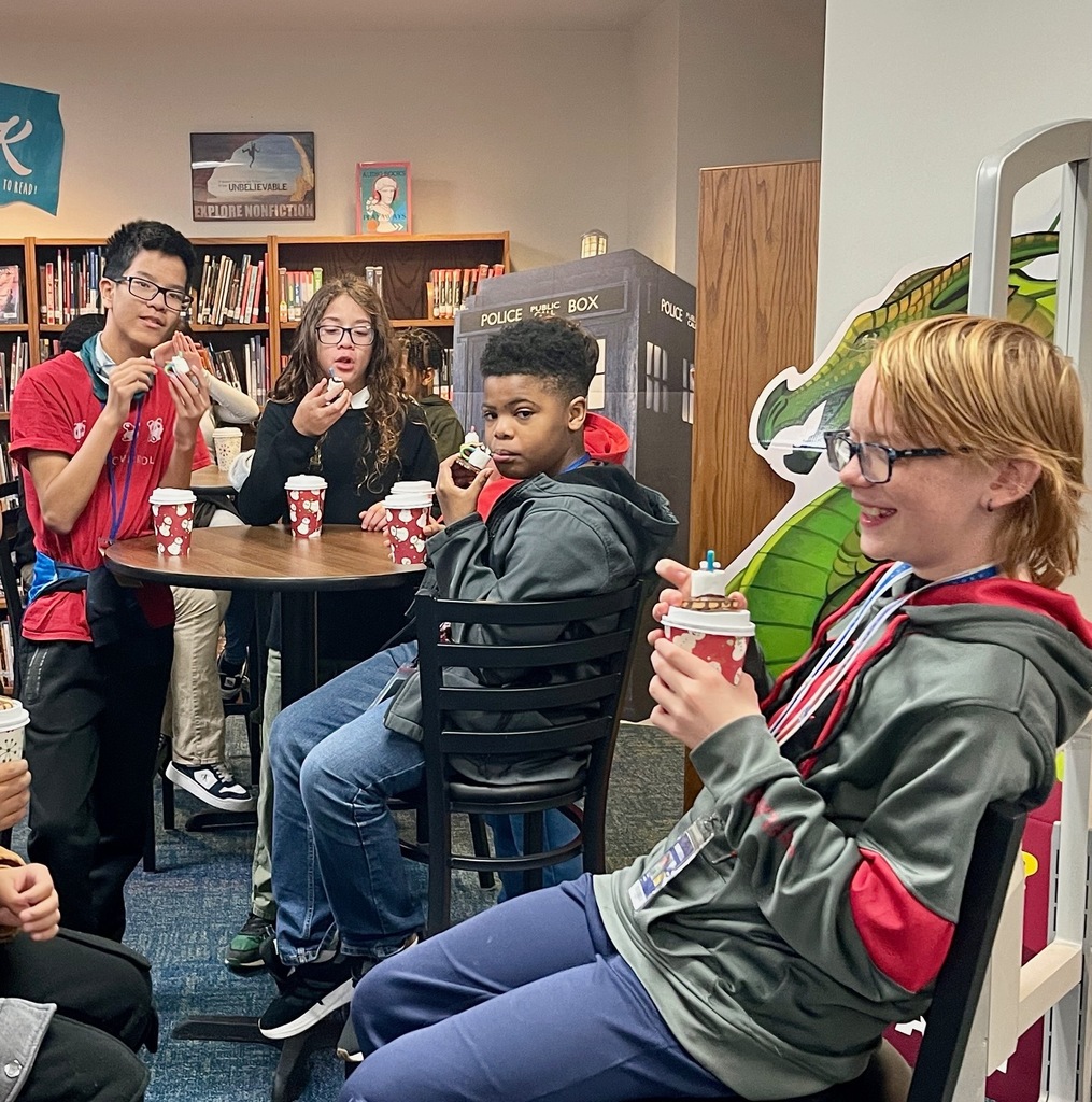 Small group of boys sit and sip hot chocolate at a table during the Starbooks Book Tasting event in the library.