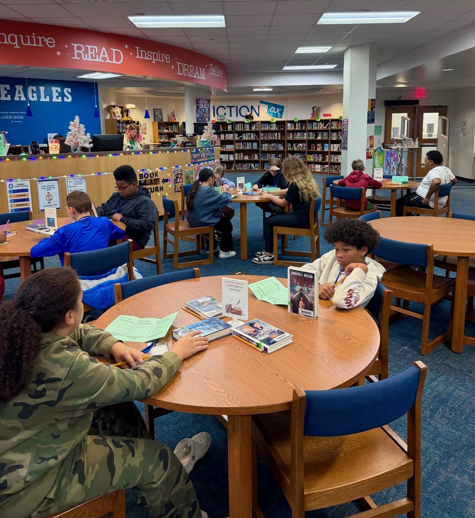 Students sit at tables in the library exploring books of different genres as part of a Book Tasting event.