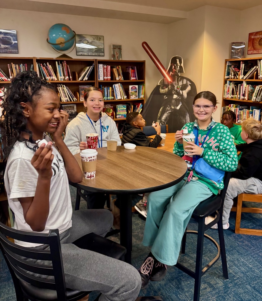 Three girls sit at a table and sip hot chocolate as part of the Starbooks Book Tasting event in the library.