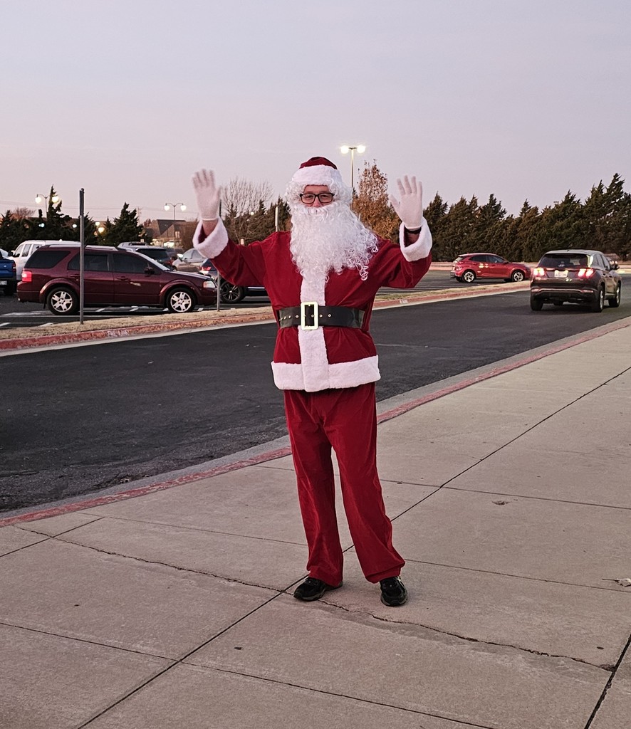 Santa waving at the camera with a drive and parking lot in the background