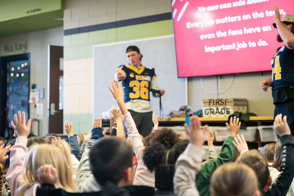 football players talking to elementary students