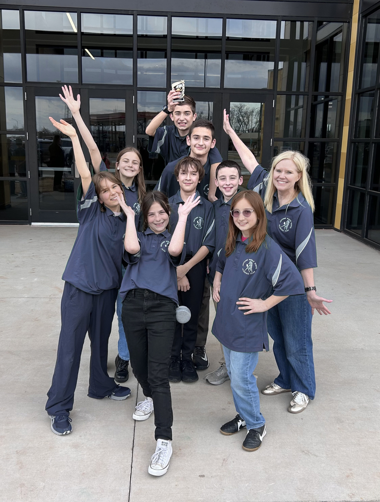 8 teens and 1 teacher in navy shirts posing with a trophy
