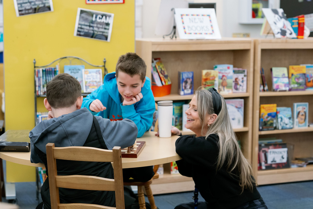 adult watching students play chess
