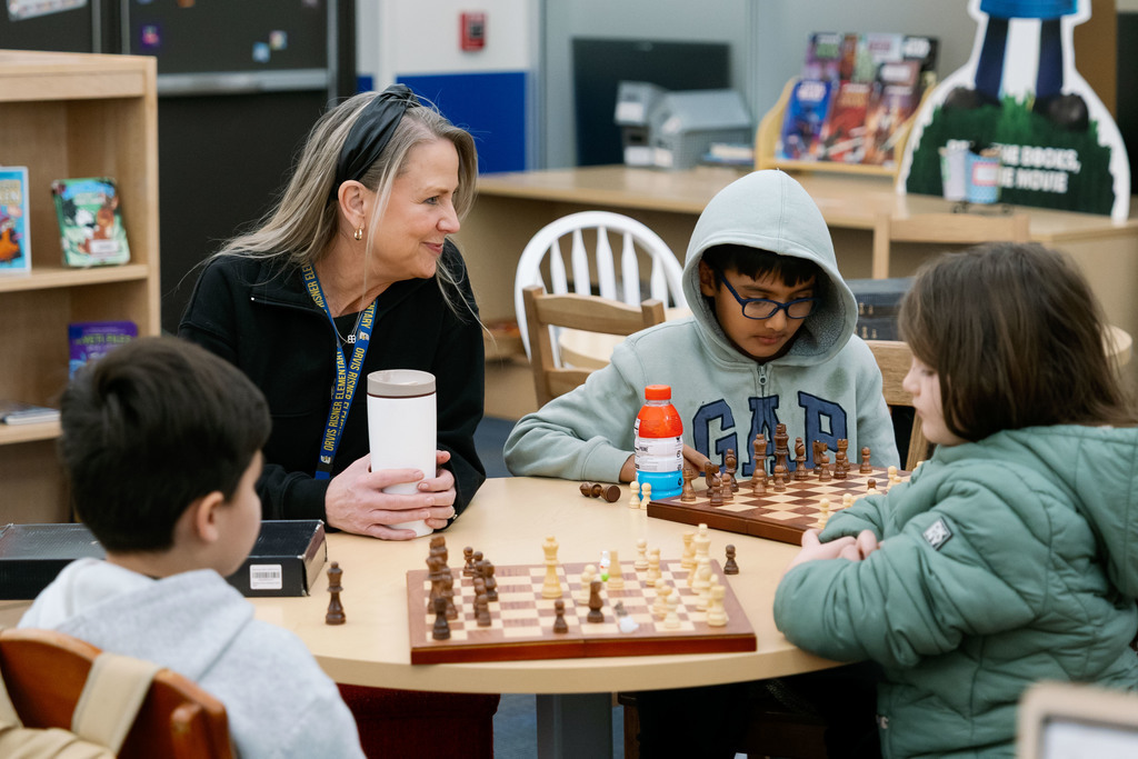 adult watching students play chess