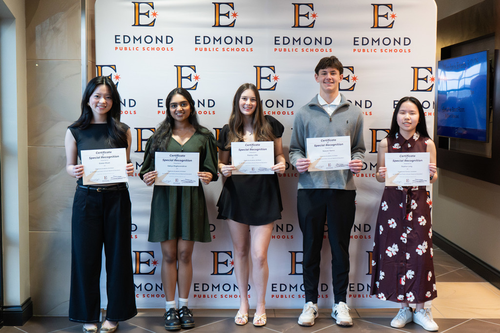 students standing with their awards against a backdrop at a board meeting
