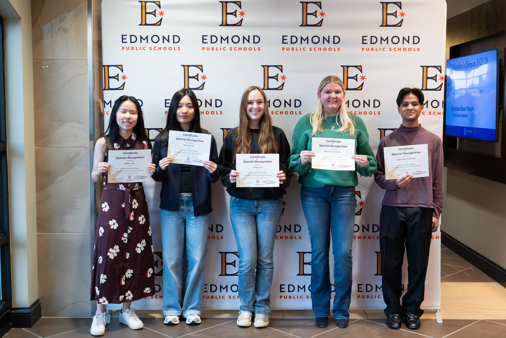 students standing with their awards against a backdrop at a board meeting