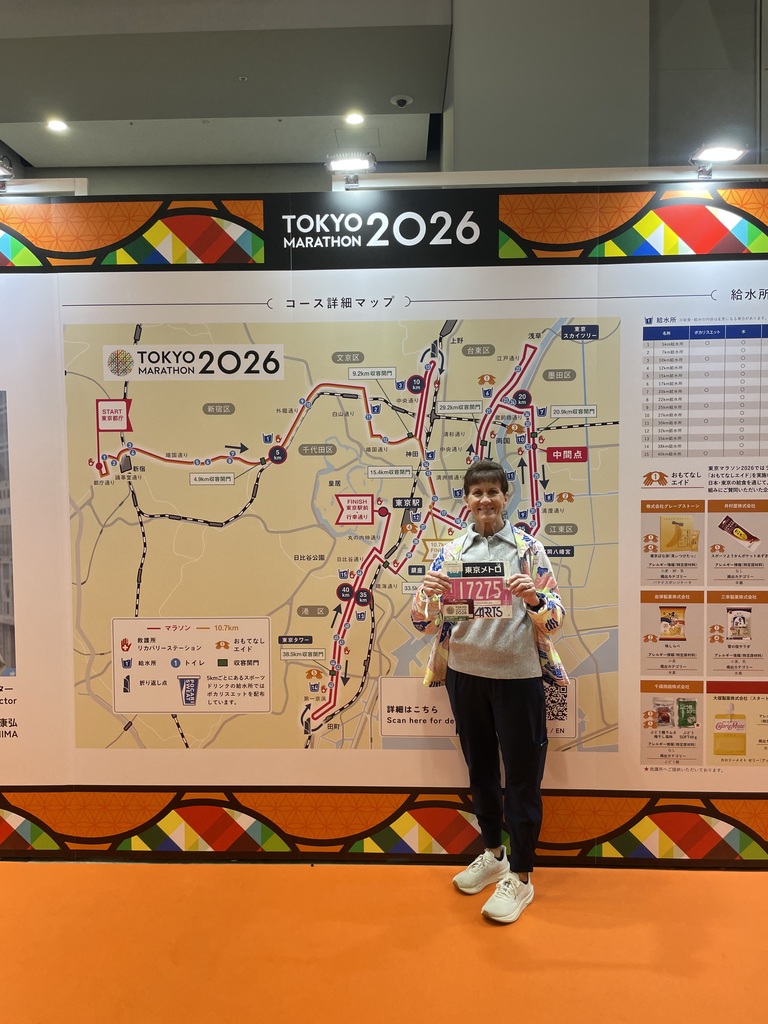 Ms. Mary holds her race bib in front of the route map for the 2026 Tokyo Marathon.