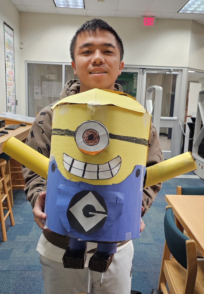 A teen boy holding a 3-D object that looks like a character from Minions