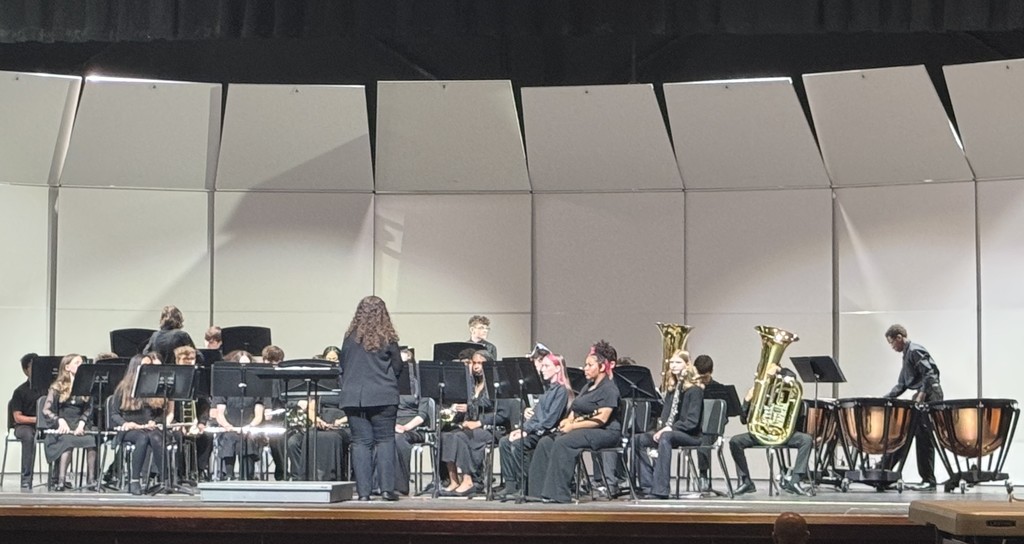 Mrs. JoeLee Mills standing in front of students holding band instruments on a stage