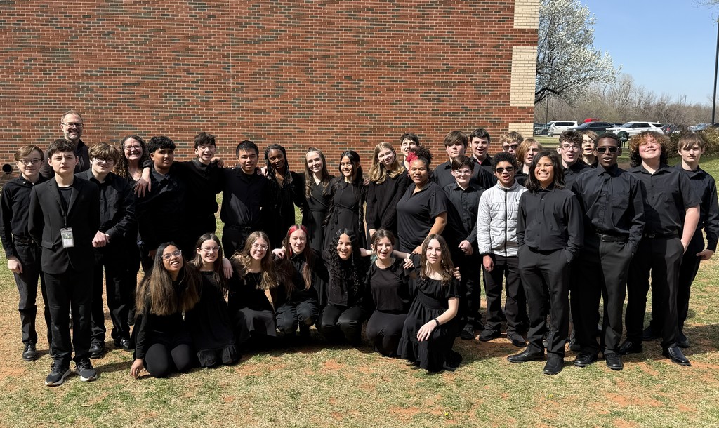 A group of students and 2 teachers wearing black and posing in front of a red brick wall