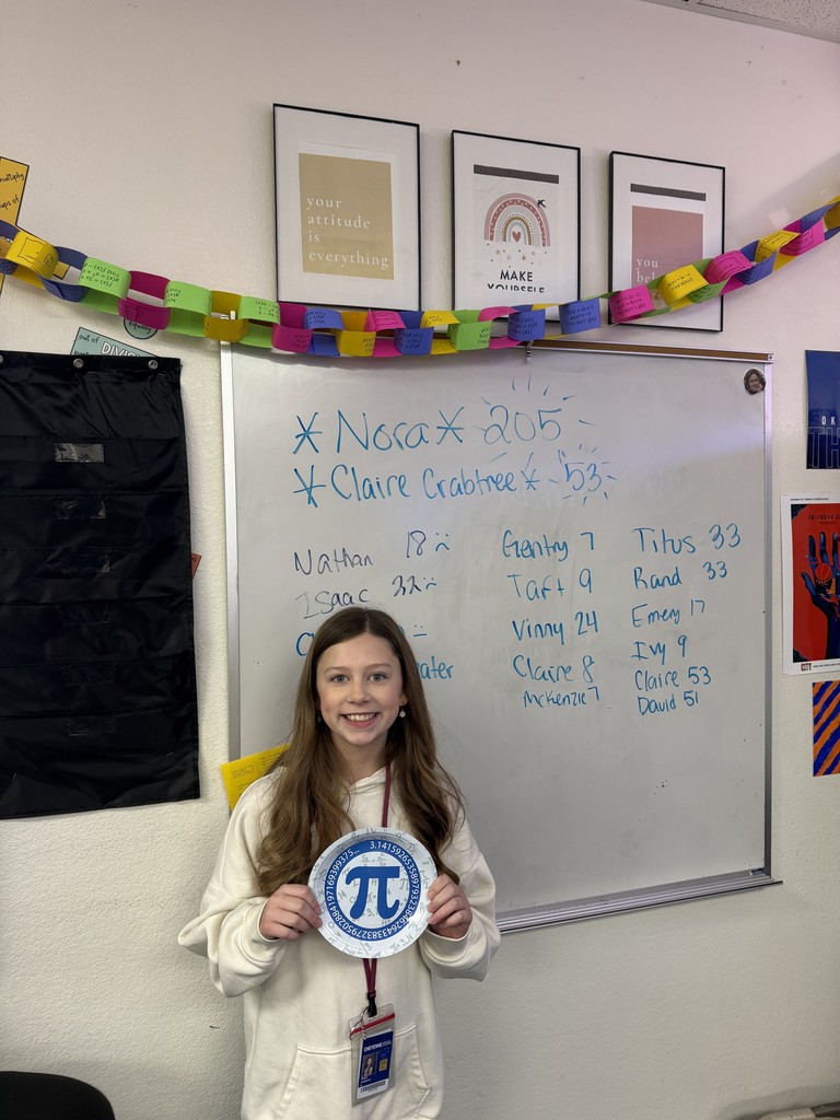 A girl standing in front of a white board holding a circle with the Pi symbol on it.