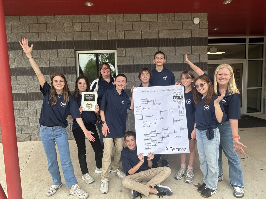 8 students and two female teachers posing with a bracket sign in front of a grey and red brick building