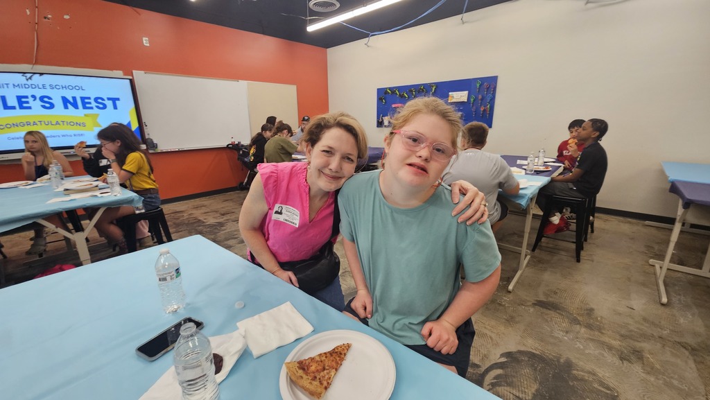 Mom puts her arm around the shoulder of her daughter and both smile for the camera as they enjoy eating lunch together.