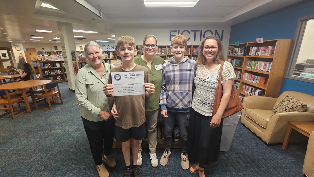 Group of family members stand next to a student as he holds up his Eagles Nest certificate.