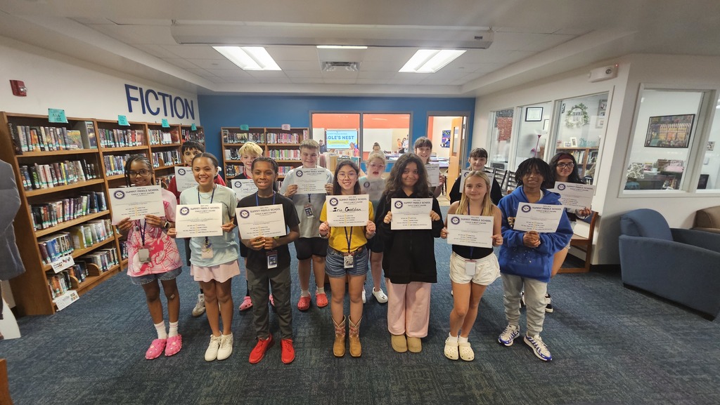 Large group of 6th grade students stand in rows and smile as they hold up Eagles Nest certificates.