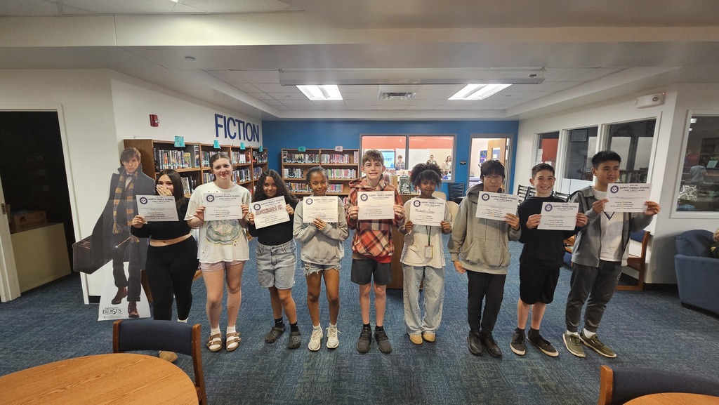 Large group of 8th grade students stand in rows and smile as they hold up Eagles Nest certificates.