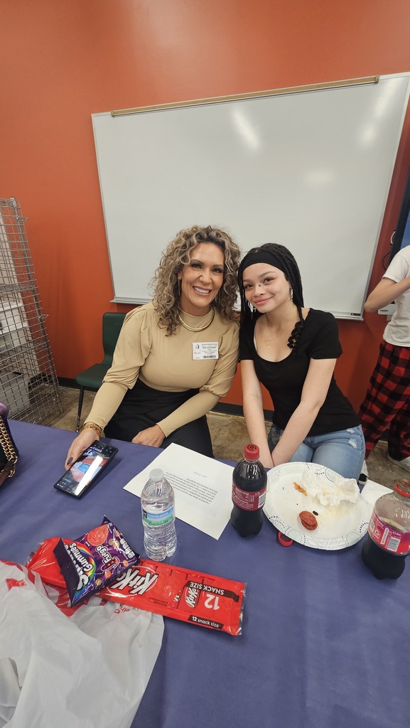 Student and family member smile as they sit at a table eating lunch together. 