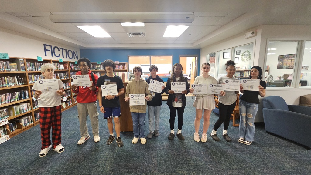 Large group of 7th grade students stand in rows and smile as they hold up Eagles Nest certificates.