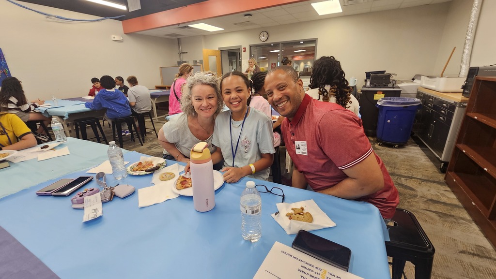 Student sits in between parents as they all smile directly at the camera. 