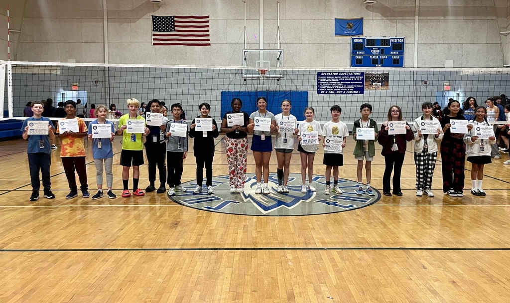 6th grade Student of the Month recipients stand at midcourt in the Summit gym and smile for the camera while holding up their certificates.