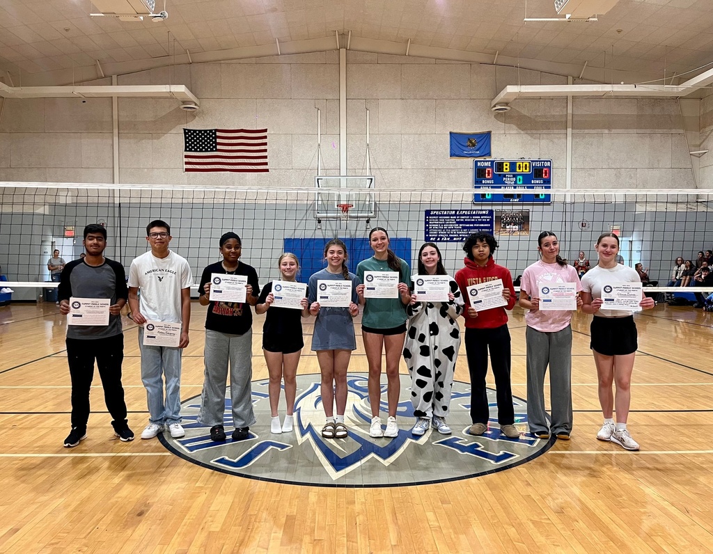 8th grade Student of the Month recipients stand at midcourt in the Summit gym and smile for the camera while holding up their certificates.