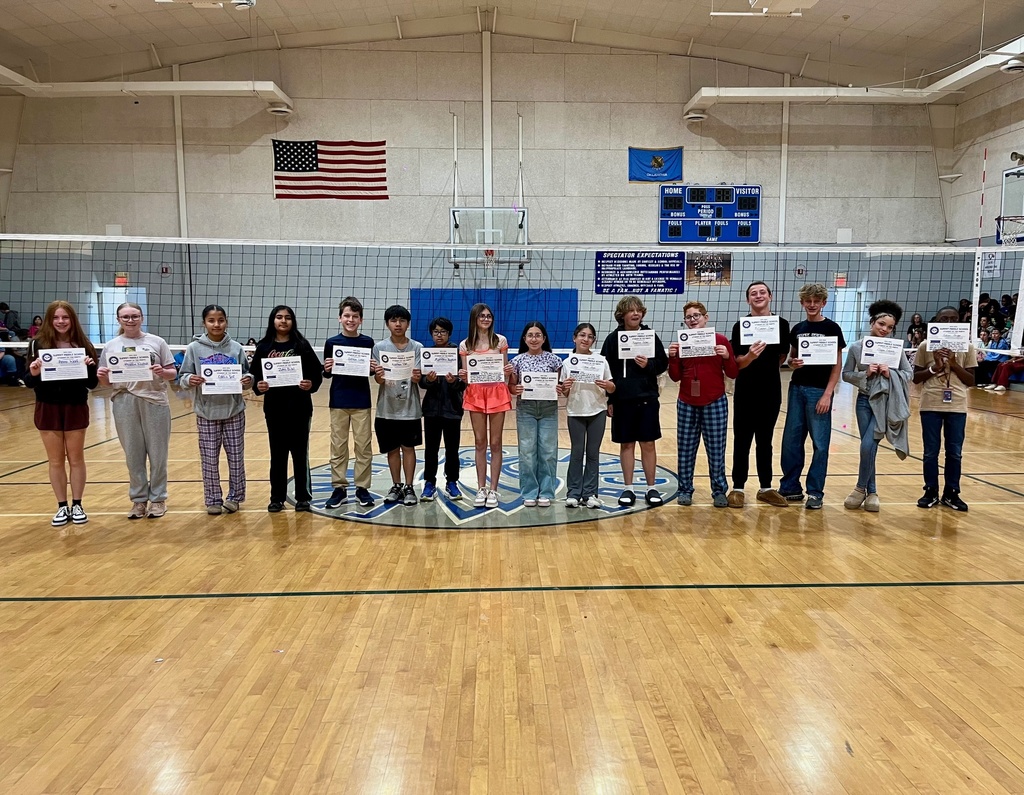 7th grade Student of the Month recipients stand at midcourt in the Summit gym and smile for the camera while holding up their certificates.