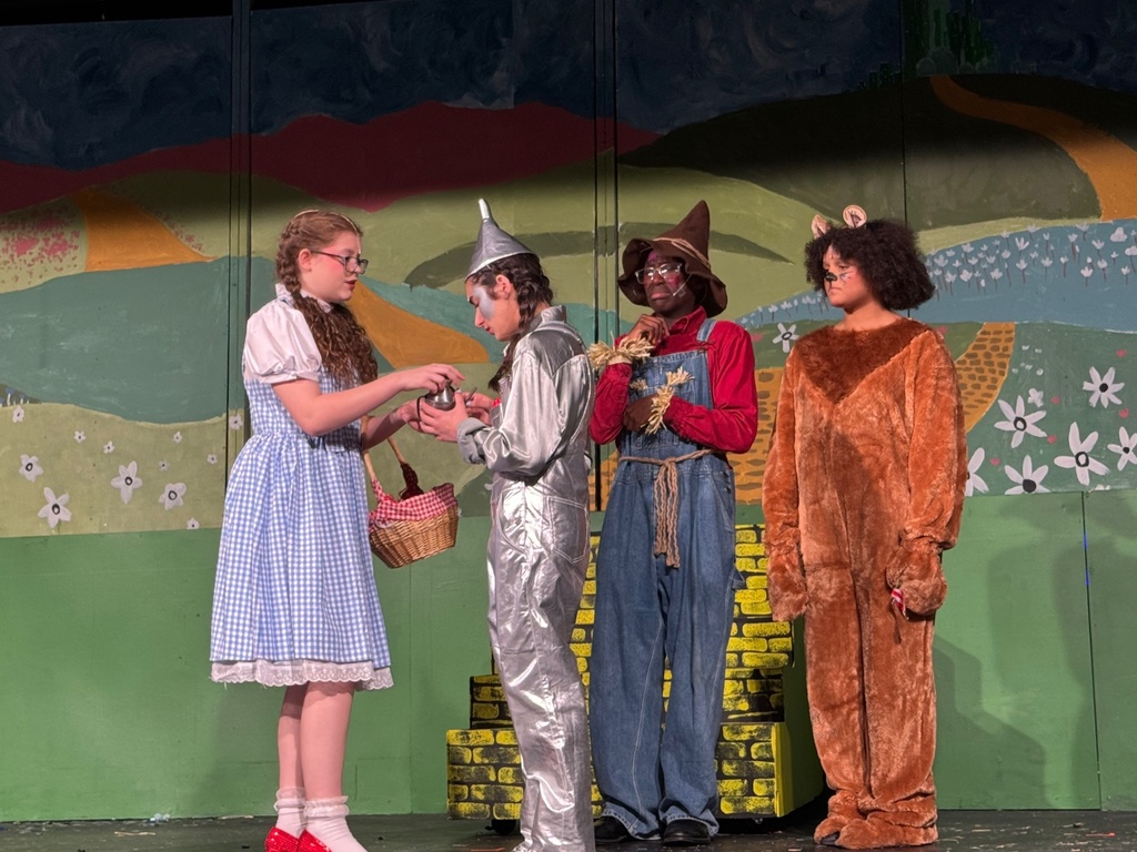 Students on stage dressed as Dorothy, the Tin Man, the Scarecrow, and the Cowardly Lion