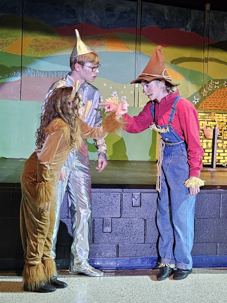 The Cowardly Lion, the Tin Man, and the Scarecrow standing next to the stage