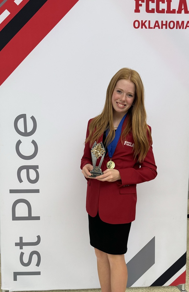 Elizabeth stands in front of a white 1st place sign while holding a trophy and wearing a 1st place metal and smiling for the camera.