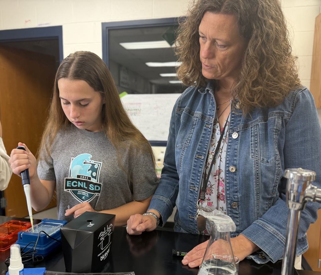teacher watching a student conduct an experiment