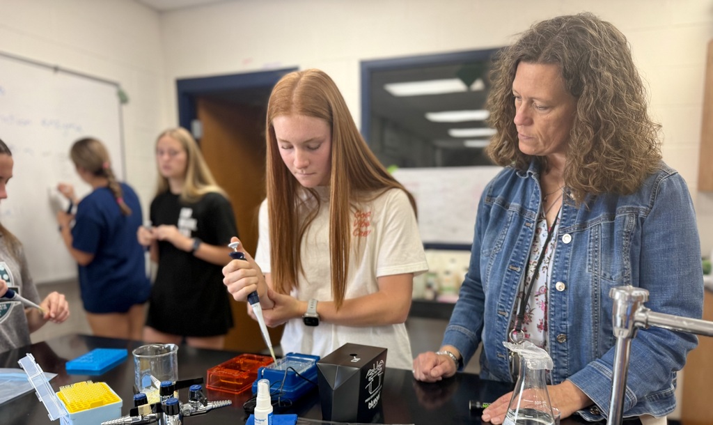 teacher watching a student conduct an experiment