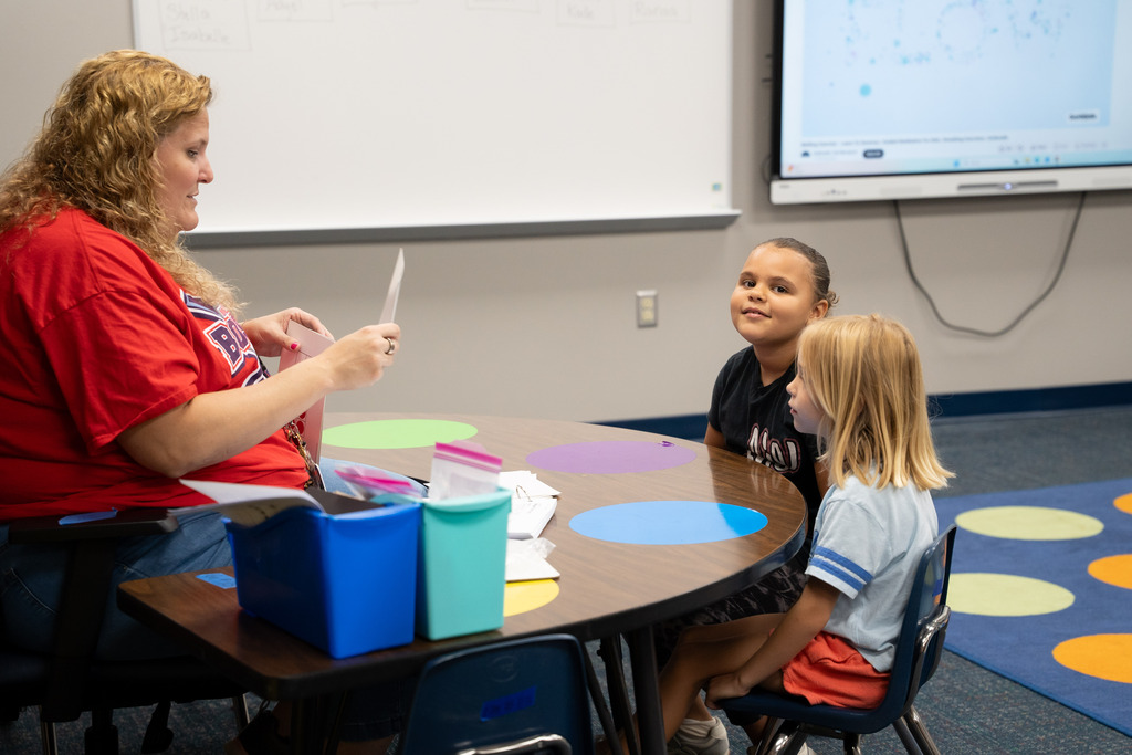 teacher and students sitting at a table working on an assignment together