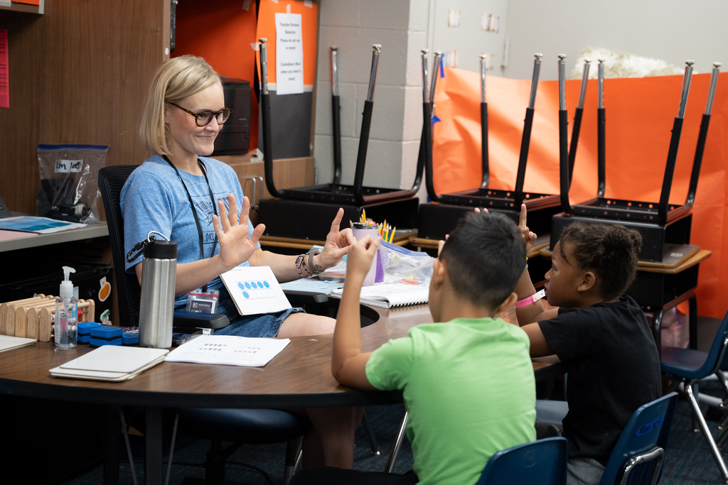 teacher and students sitting at a table working on an assignment together