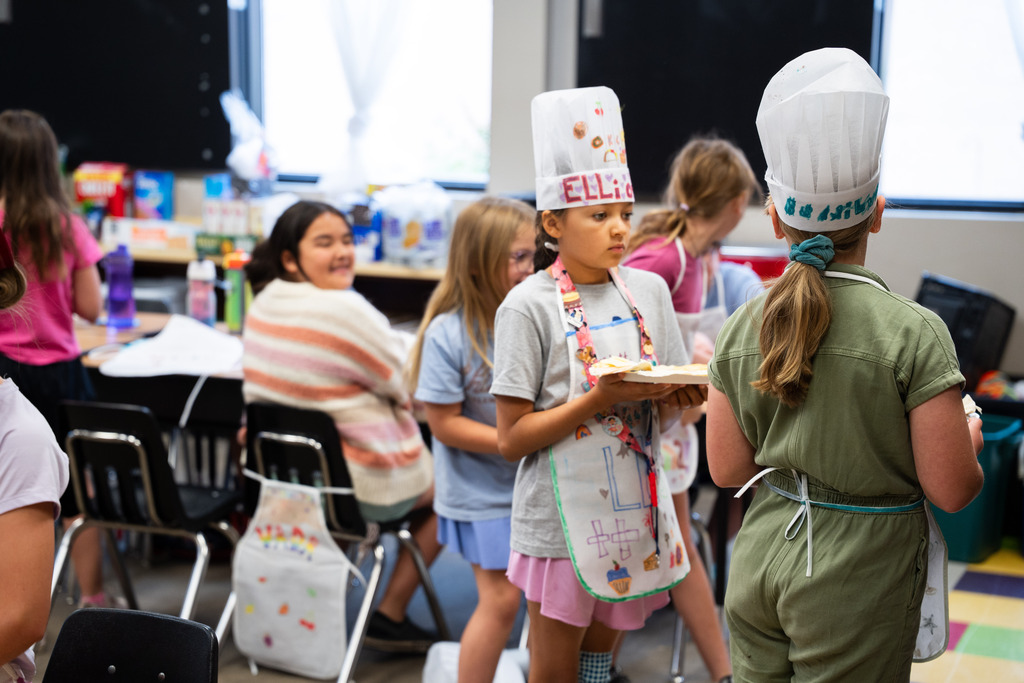 students in chef outfits and hats taking a cooking class