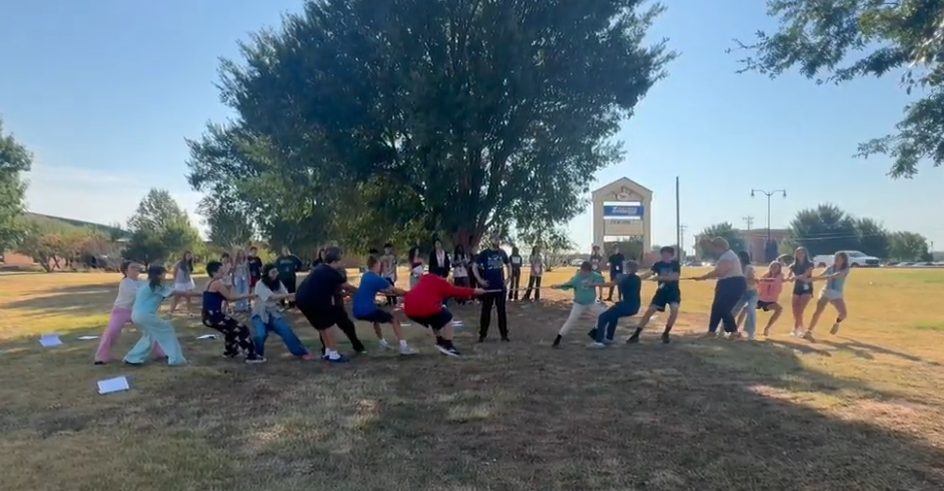 Teen boys and girls playing tug of war with a long rope outdoors