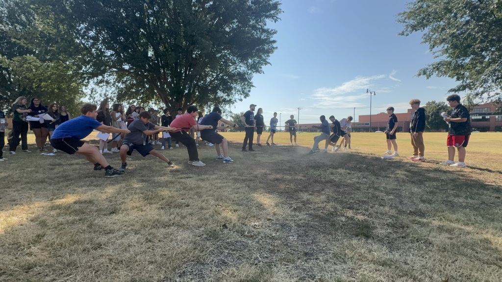 Teens playing tug-of-war outdoors while other students watch